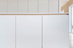 Minimalistinen valkoinen keittiö hirsitalossa. Massiivikoivuinen profiilijärjestelmä lämmittää kalusteet.